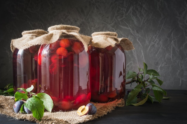 Three homemade canned plum compote in large jars on wooden board Rustic style
