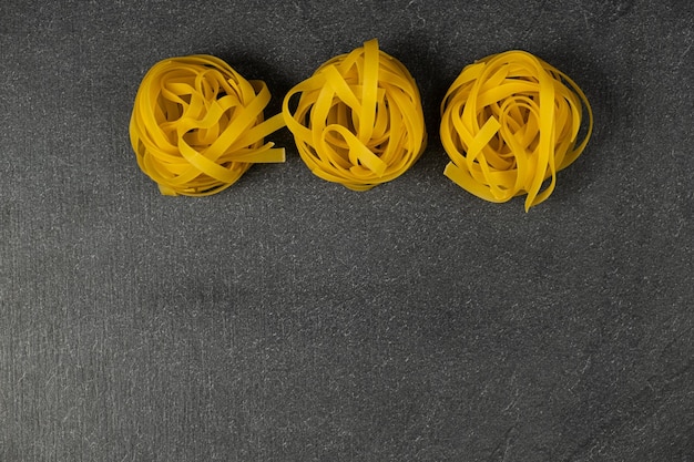 Three homemade fettuccine nest isolated on dark background