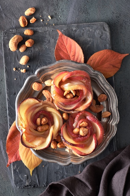 Three homemade puff pastries with rose shaped apple slices on metal plate on dark