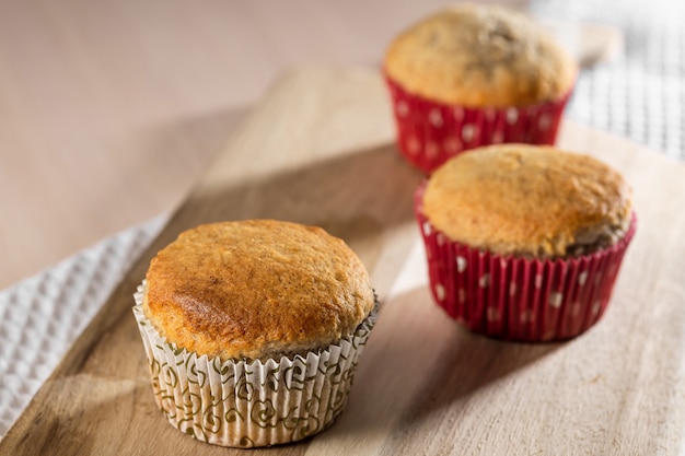 Three homemade tasty muffins on wooden board close up
