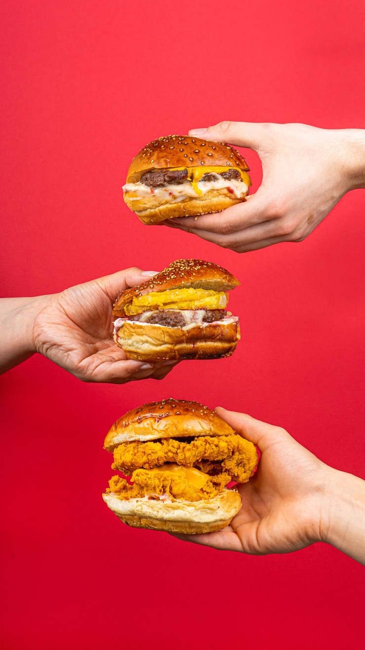 Three human hands holding tasty hamburgers cheeseburger burger isolated on red background