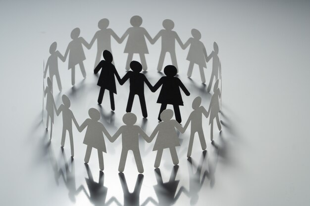 Photo three human paper figures surrounded by circle of paper people holding hands