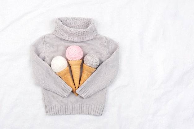 Three ice cream from ball of yarn in waffle cones and gray knitted sweater on white background. Top view Flat lay Copy space.