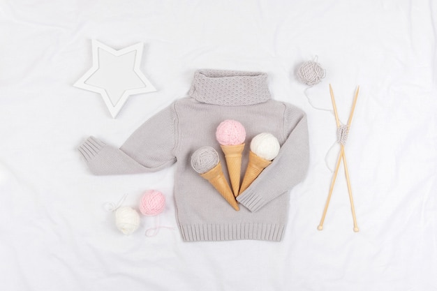 Three ice cream from yarn and waffle cones on a gray knitted sweater, wooden knitting needles and star on white background. Knitting, hobby and handmade concept. Top view Flat lay.