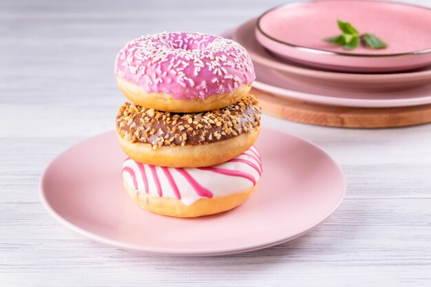 Three iced donuts stacked on a pink ceramic plate