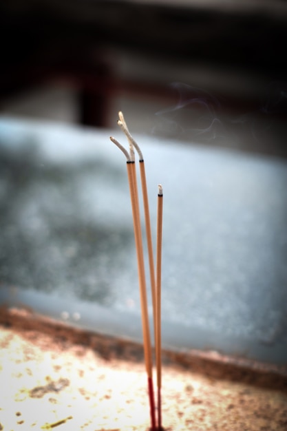 three incense sticks or joss sticks flaming and burning with smoke  in a Buddhism temple