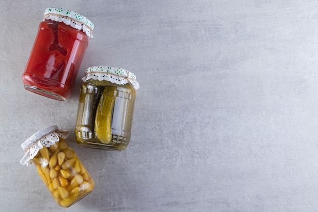 Three jars of pickled vegetables placed on stone table.