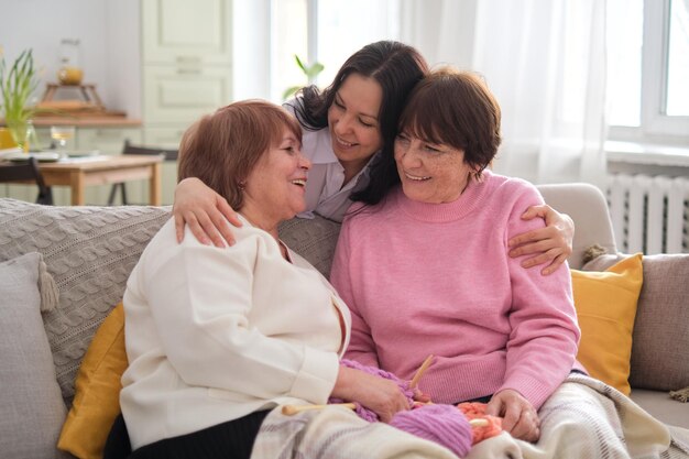 異なる世代の 3 人の陽気な女性が、快適な居住空間で心からの会話を交わし、抱擁を交わし、笑い合う。精神的健康と幸福において家族の強い絆を築く役割を果たしている。