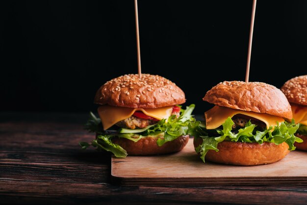 Three juicy hamburgers with meat, cheese, lettuce, tomato on a wooden Board