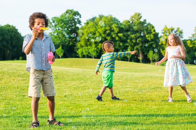 Photo three kids on the glade with soap bubble.