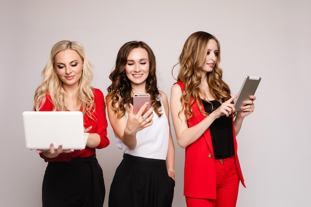 Three ladies using gadgets Three gorgeous elegant young women in casual clothe