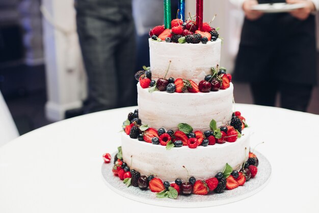 Three-layered wedding cake with fresh berries.Decorated with strawberry, blueberry, cherry and blackberry.