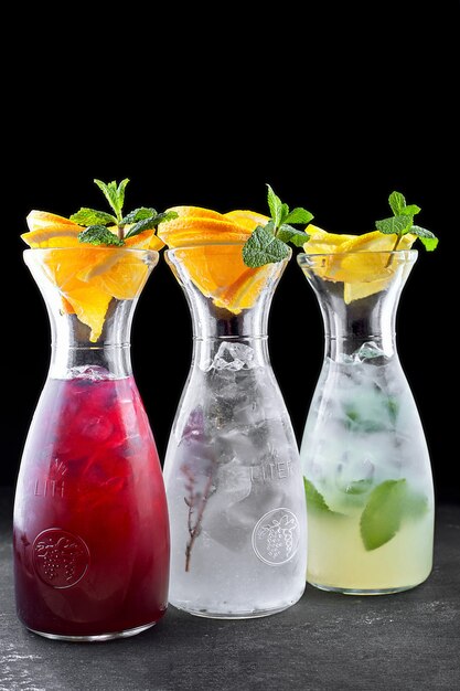 Three lemonades, lime, cucumber, strawberry, in transparent jugs, on a black table