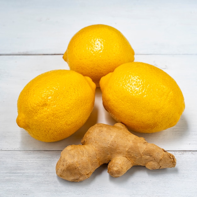 Tre limoni e radice di zenzero su fondo di legno bianco