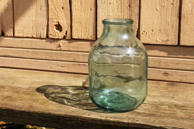 A three-liter jar stands on a wooden bench near the house.