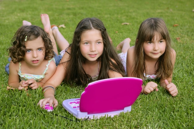 Photo three little girl playing with toy computer in grass