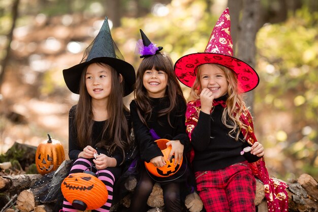 Three little girls in halloween witch costumes laugh conjure walk through the autumn forest