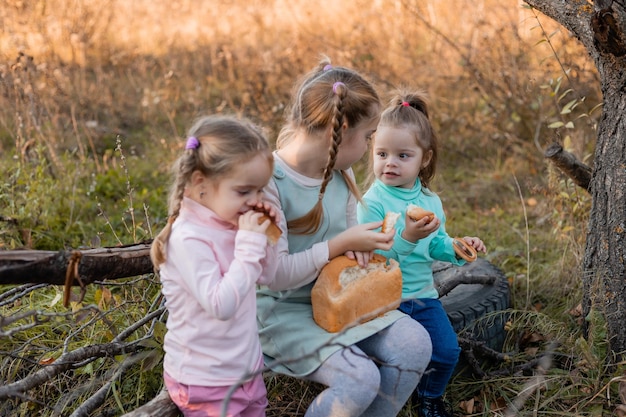 3 人の少女が秋の森でピクニックを持っているし、パンを食べている子供たちが屋外を歩く