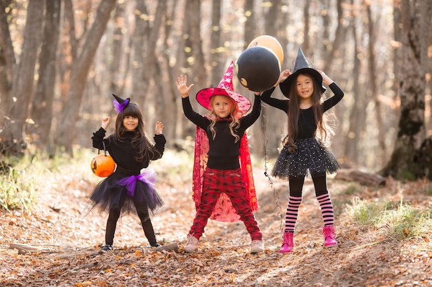 魔女の衣装を着た3人の少女が笑い、秋の森のハロウィーンのコンセプトを歩きます