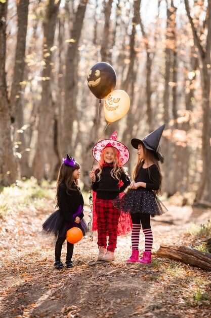 Three little girls in witch costumes laugh walk through the autumn forest with baskets for sweets