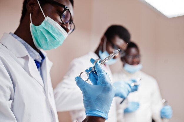 Three male doctors colleagues with tools at hands in clinic. Close up of syringe for injections.