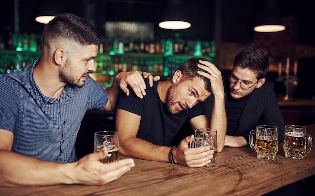 Three male friends in the bar Supporting sad friend Unity of people With beer on the table