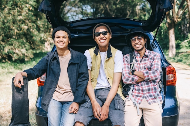Трое друзей-мужчин улыбаются и сидят в багажнике машины, готовые к поездке