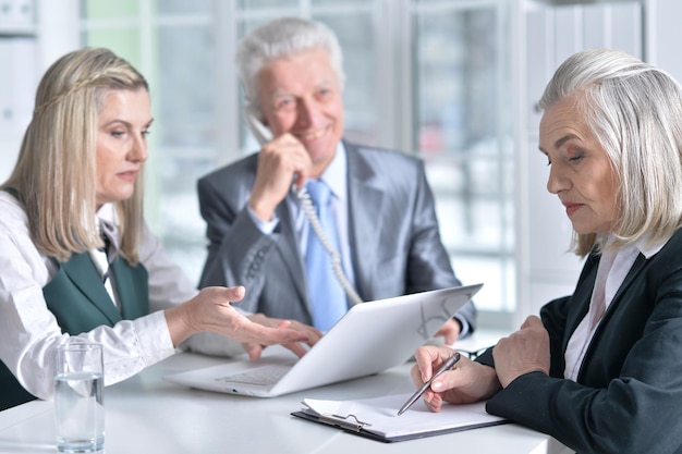 Three mature businesspeople using laptop and chatting