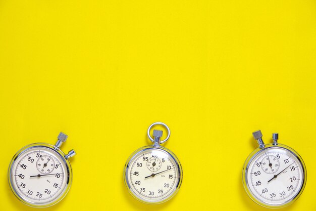 Three mechanical stopwatches on a yellow background.