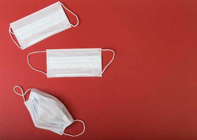 Three medical masks one used and two unused are on an isolated red background