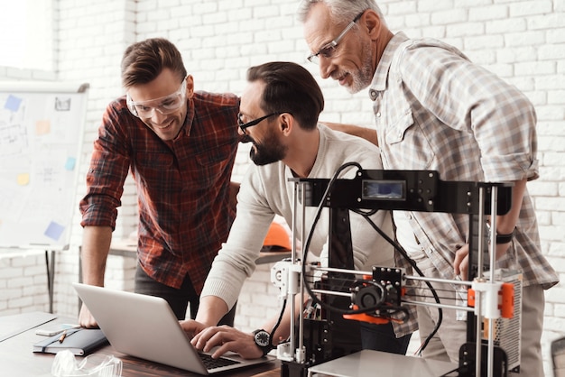 Three men are working on preparing a 3d printer for printing.