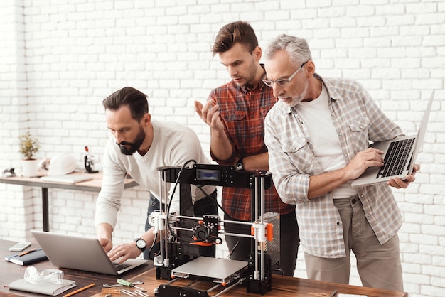 Three men are working on preparing a 3d printer.