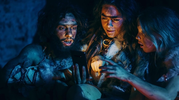 Three men in a dark room with a lit up cell phone in their hands.