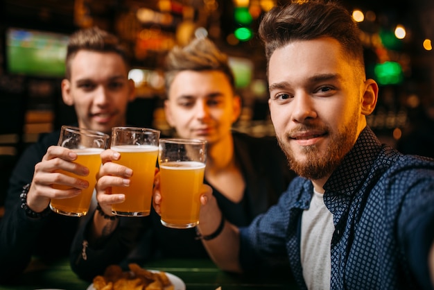 Tre uomini hanno alzato i bicchieri con la birra per la vittoria in un bar sportivo, felici tifosi di calcio