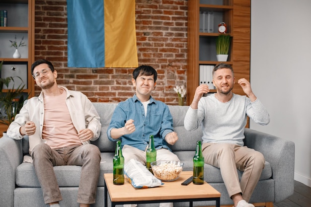 Three men watching a football game on tv and drinking a beer