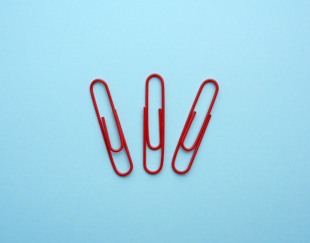 Three metal red paper clips on a blue background