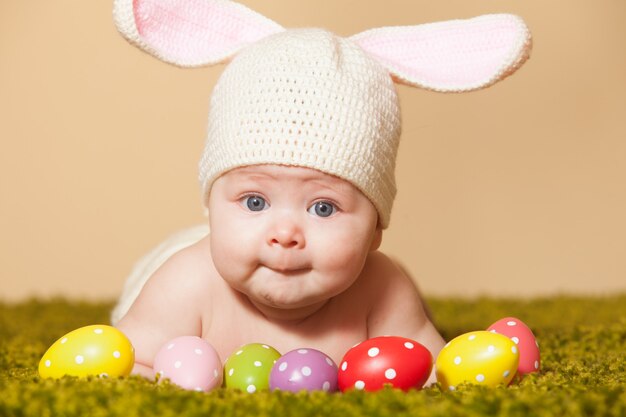 Three months baby lying on his stomach as a Easter bunny on the grass with eggs