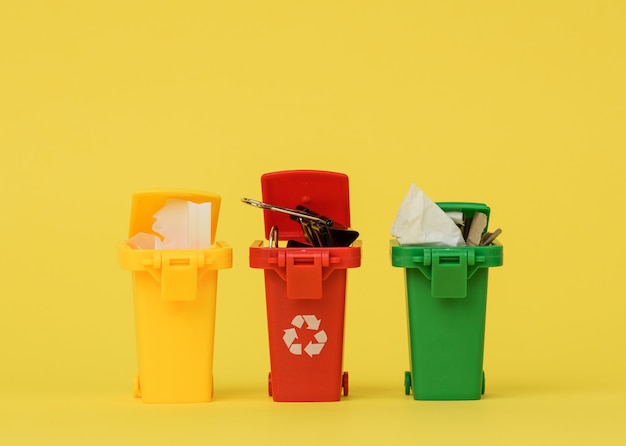 Three multi-colored plastic containers on a yellow surface, the concept of correct sorting of garbage for further recycling