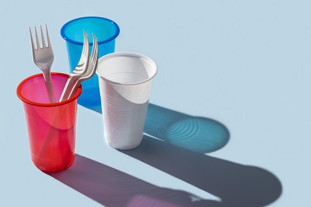 Tre bicchieri di plastica multicolori, posate su sfondo blu. ombre lunghe.