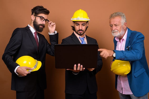 Three multi ethnic bearded businessmen together against brown wall