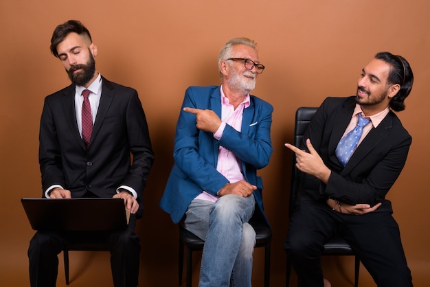 Three multi ethnic bearded businessmen together against brown wall