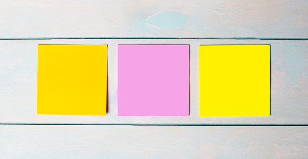 Photo three multicolored blank stickers with a place to insert text on a light blue blue wooden background copy space