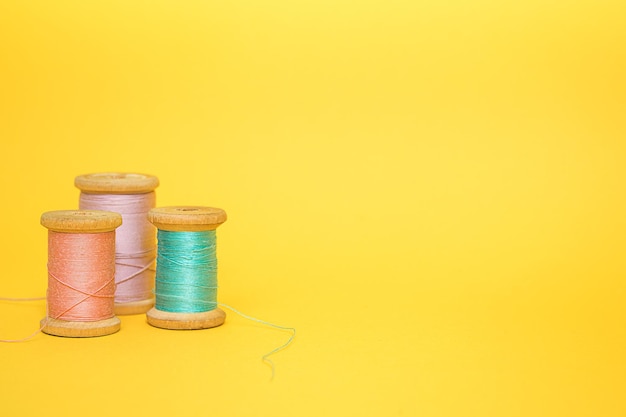 Three multicolored spools of thread on a yellow background