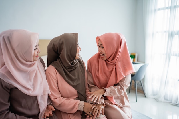 Three Muslim women chatting while sitting on the bed