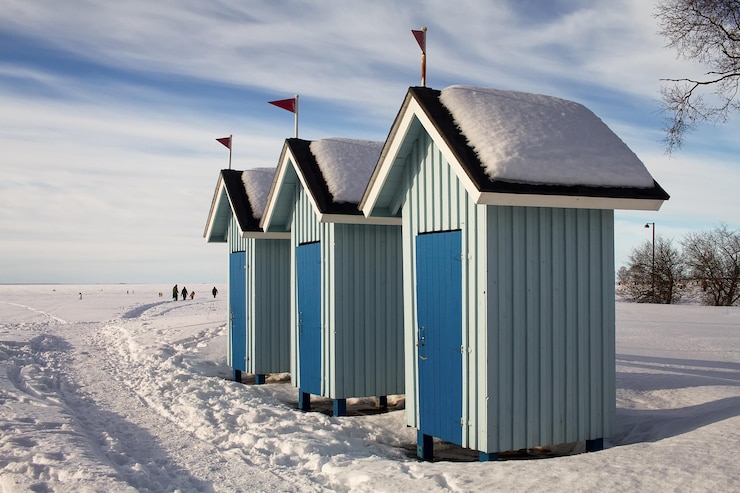 Photo three old beach huts stand empty on a beautiful winter day people are walking on the ice