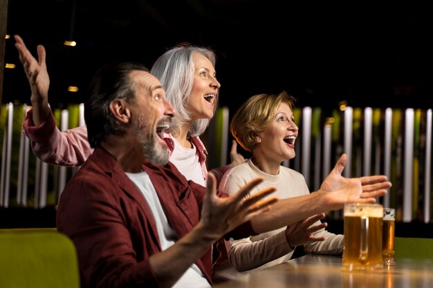 Foto tre amici più grandi che bevono e fanno il tifo in un ristorante