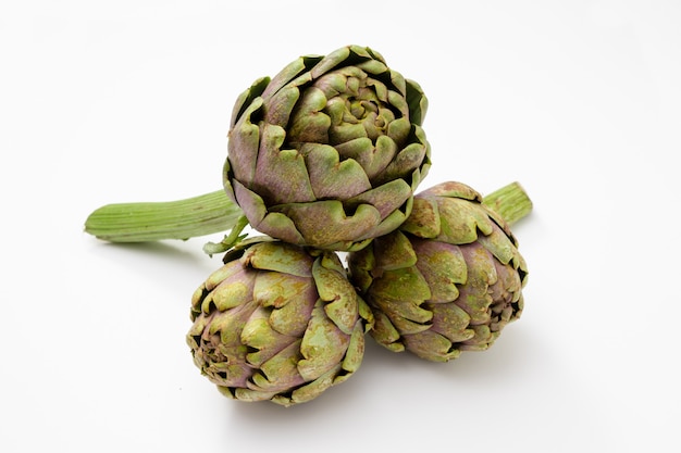 Three organic and fresh artichokes with a piece of stem on a white surface.