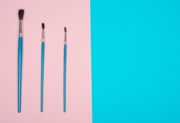 Three paintbrushes on pink and blue 