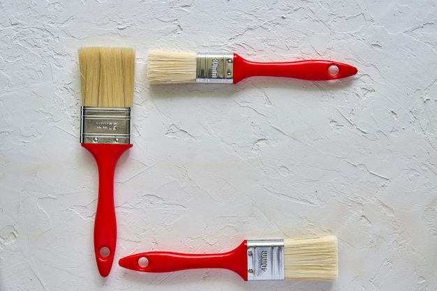 Three paintbrushes with red handles on freshly made concrete background. Repairing concept. Top view with copy space