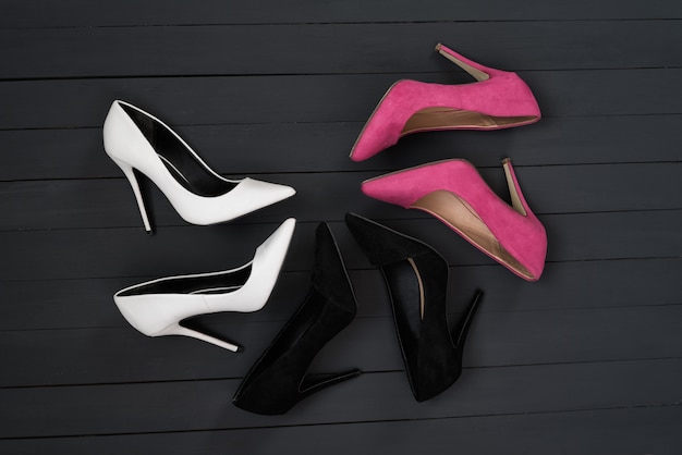 Three pairs of different high heel shoes. Black wooden background.